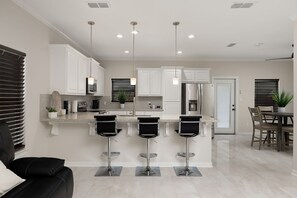 A modern kitchen with white cabinets, stainless steel appliances, and three black bar stools.