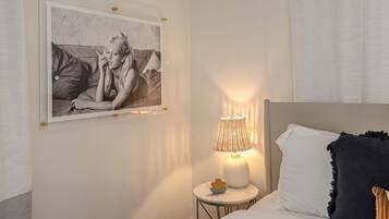 Un dormitorio con una cama, una mesita de noche con lámpara y un cuadro en la pared.