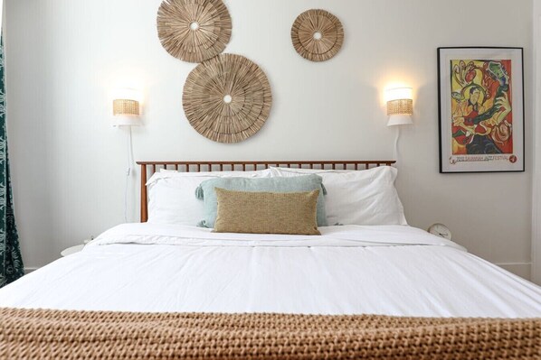 A bed with white bedding, two wall-mounted lamps, and a framed artwork on the wall.