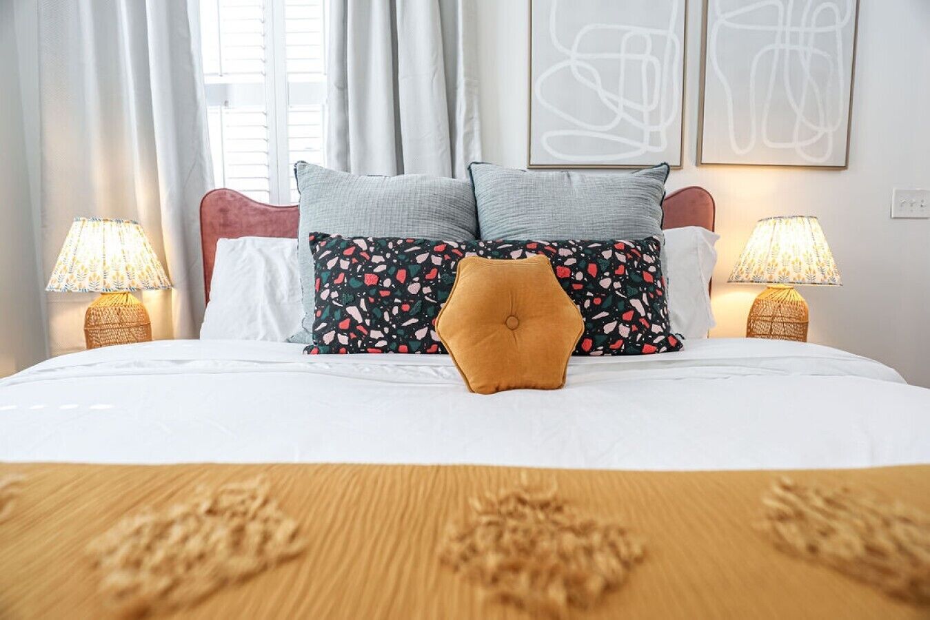 Ein Hotelzimmer mit Bett, zwei Nachttischlampen, einem Fenster mit Vorhängen und abstrakter Wandkunst.