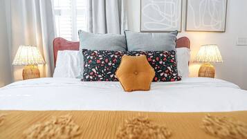 Ein Hotelzimmer mit Bett, zwei Nachttischlampen, einem Fenster mit Vorhängen und abstrakter Wandkunst.