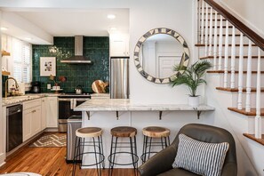 A modern kitchen with a central island, bar stools, a staircase, and a large mirror.