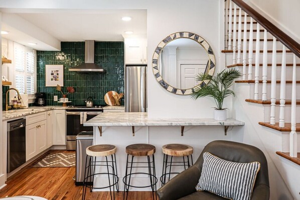 A modern kitchen with a central island, bar stools, a staircase, and a large mirror.