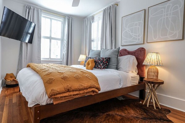A modern bedroom with a large bed, a flat-screen TV, two bedside lamps, and abstract wall art.