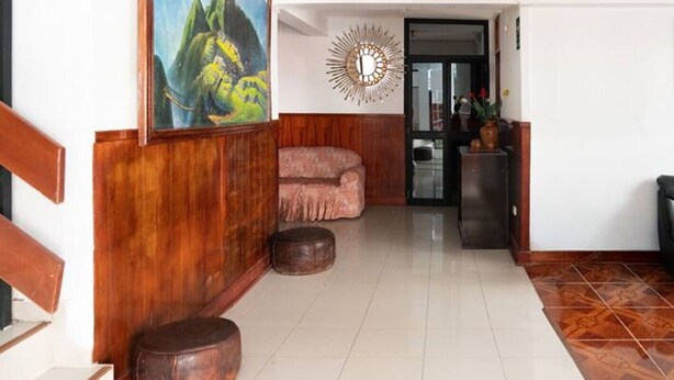 Una habitación con piso de madera, un cuadro de montañas, un sofá rosa y un espejo decorativo.
