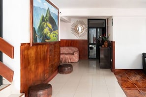 A room with a wooden floor, a painting of mountains, a pink sofa, and a decorative mirror. - Rituales Inn Romeritos (Cusco)