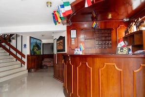 A reception desk with a wooden finish, a staircase to the left, and various flags and awards on display. - Rituales Inn Romeritos (Cusco)