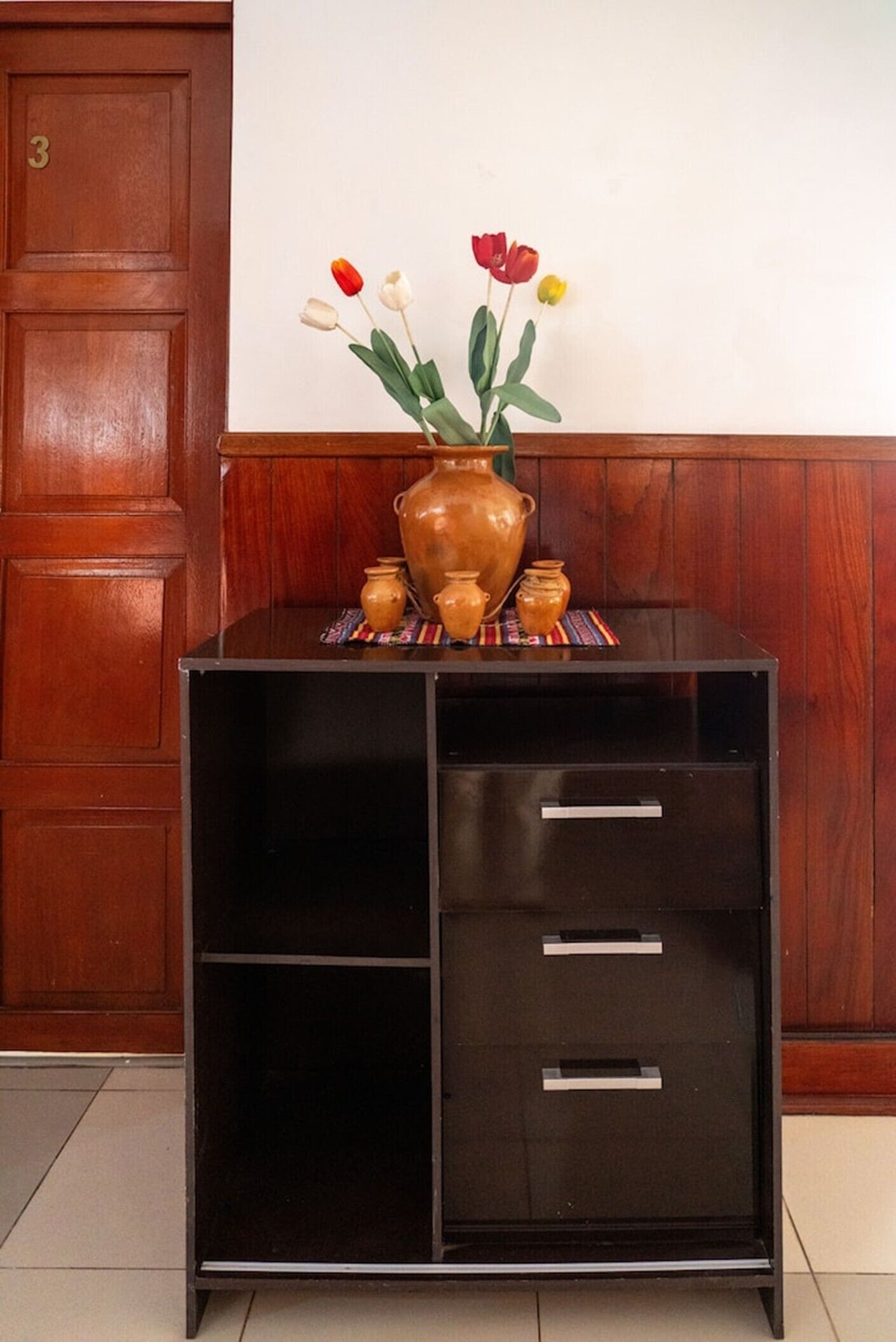 Un mueble de madera con un jarrón de flores y jarrones más pequeños encima.
