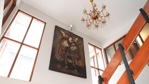 Una habitación con ventanas amplias, una araña y un cuadro en la pared.