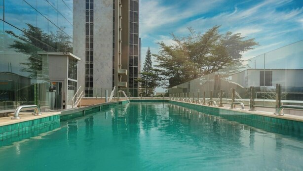 Una piscina amb aigua transparent de color blau, envoltada per una tanca, al costat d'un edifici alt amb façana de vidre.