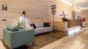 Zona de recepció d'hotel amb taulell de recepció, sofà, làmpada de peu i una planta en test.