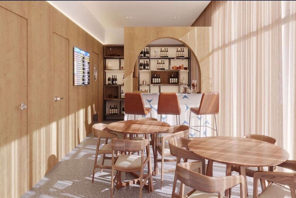 Un interior moderno con una pared de madera, una zona de bar con estantes llenos de botellas y un espacio de estar con mesas y sillas redondas.