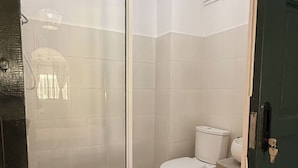 Baño con cabina de ducha, inodoro y suelo de baldosas.