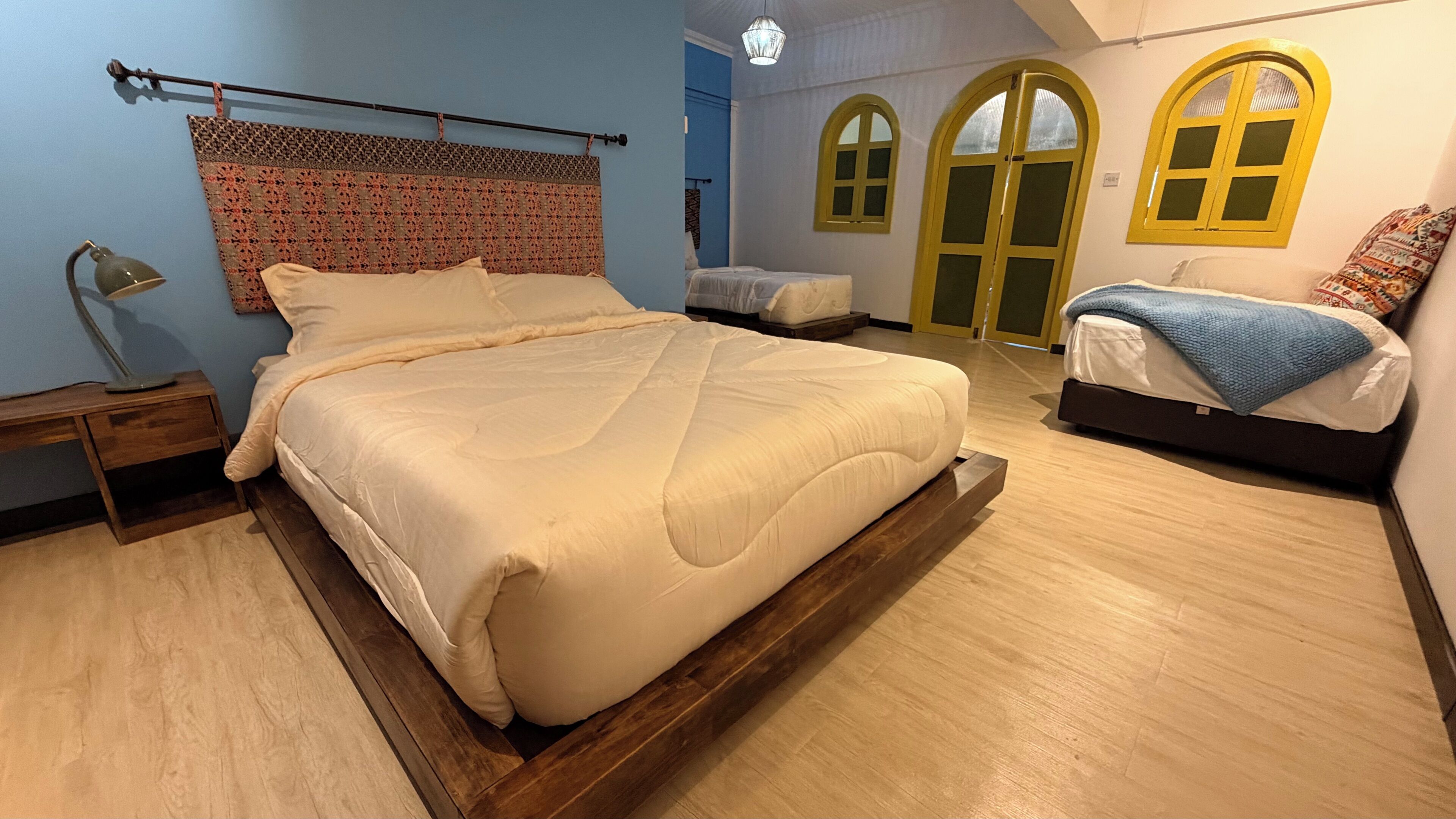 A bedroom with a large bed, a bedside table, a lamp, and two windows with yellow frames.