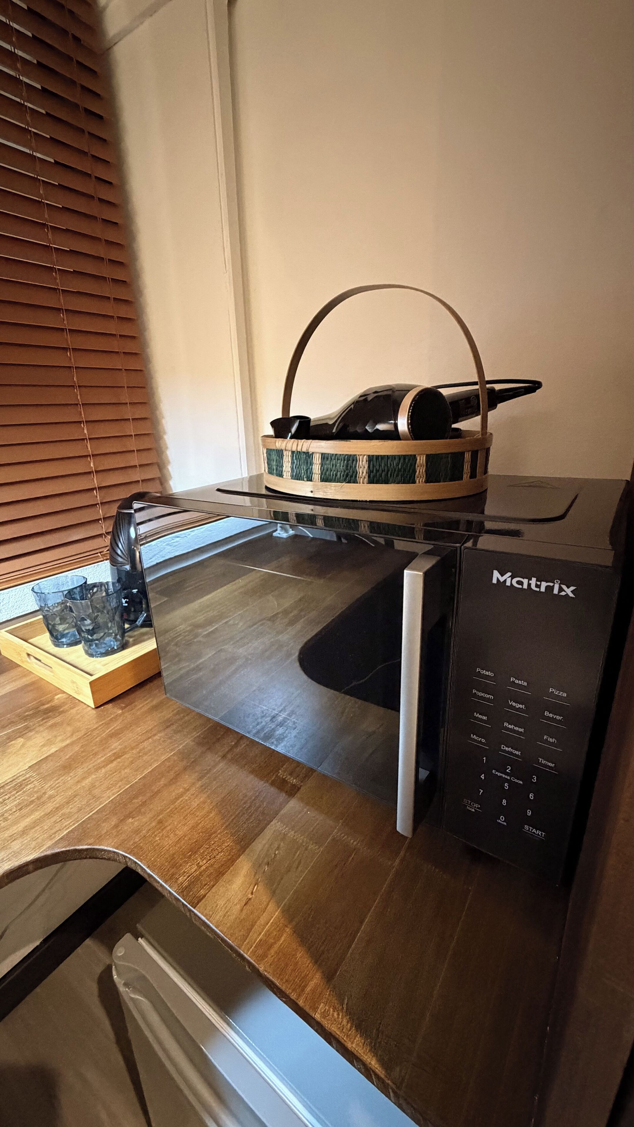 A kitchen with a microwave, a basket with a bottle, and a tray with glasses.