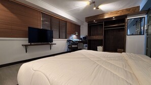 Un dormitorio con una cama, un televisor en un estante, un escritorio con una silla y un armario.