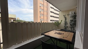 A balcony with a foosball table, a white fence, and a view of a building with multiple windows.