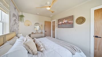 Une chambre à coucher avec un lit, un ventilateur de plafond, un téléviseur fixé au mur et une porte.