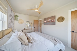 Un dormitorio con una cama, ventilador de techo, televisor en la pared y una puerta.