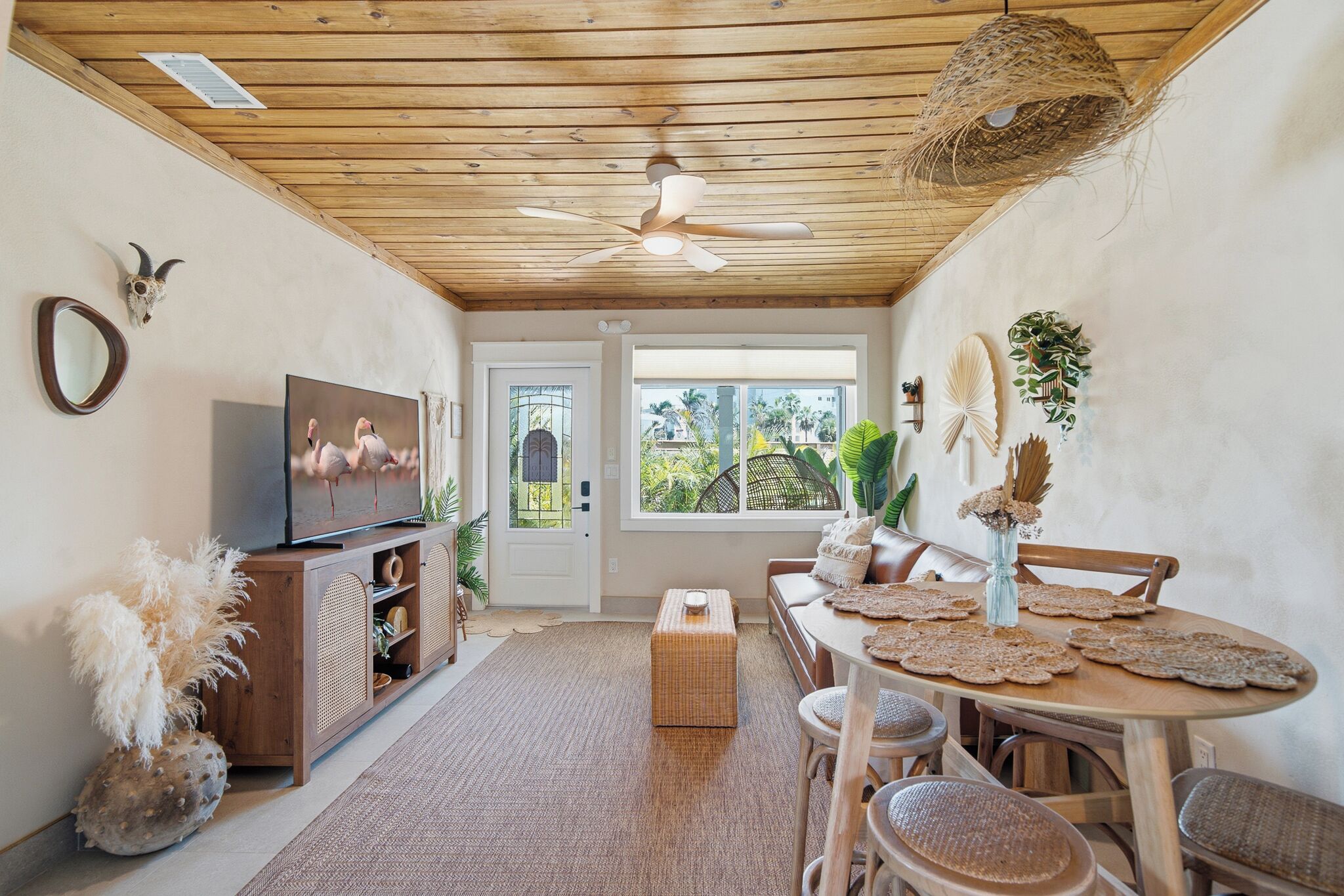 Un espace repas avec un plafond en bois, un téléviseur sur le côté gauche et une vue sur la verdure à l’extérieur.