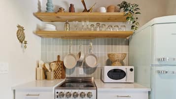 Une cuisine équipée d’une cuisinière, d’un four à micro-ondes, de casseroles suspendues et d’une étagère contenant divers ustensiles de cuisine.
