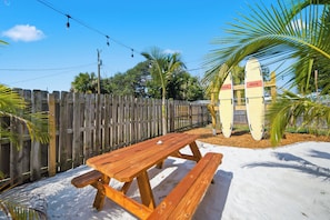 A wooden picnic table with benches, a wooden fence, and surfboards with 'RESCUE' written on them. - Cocoa Cove: Steps to Beach, Walk to Downtown, Tiki Backyard (Cocoa Beach)