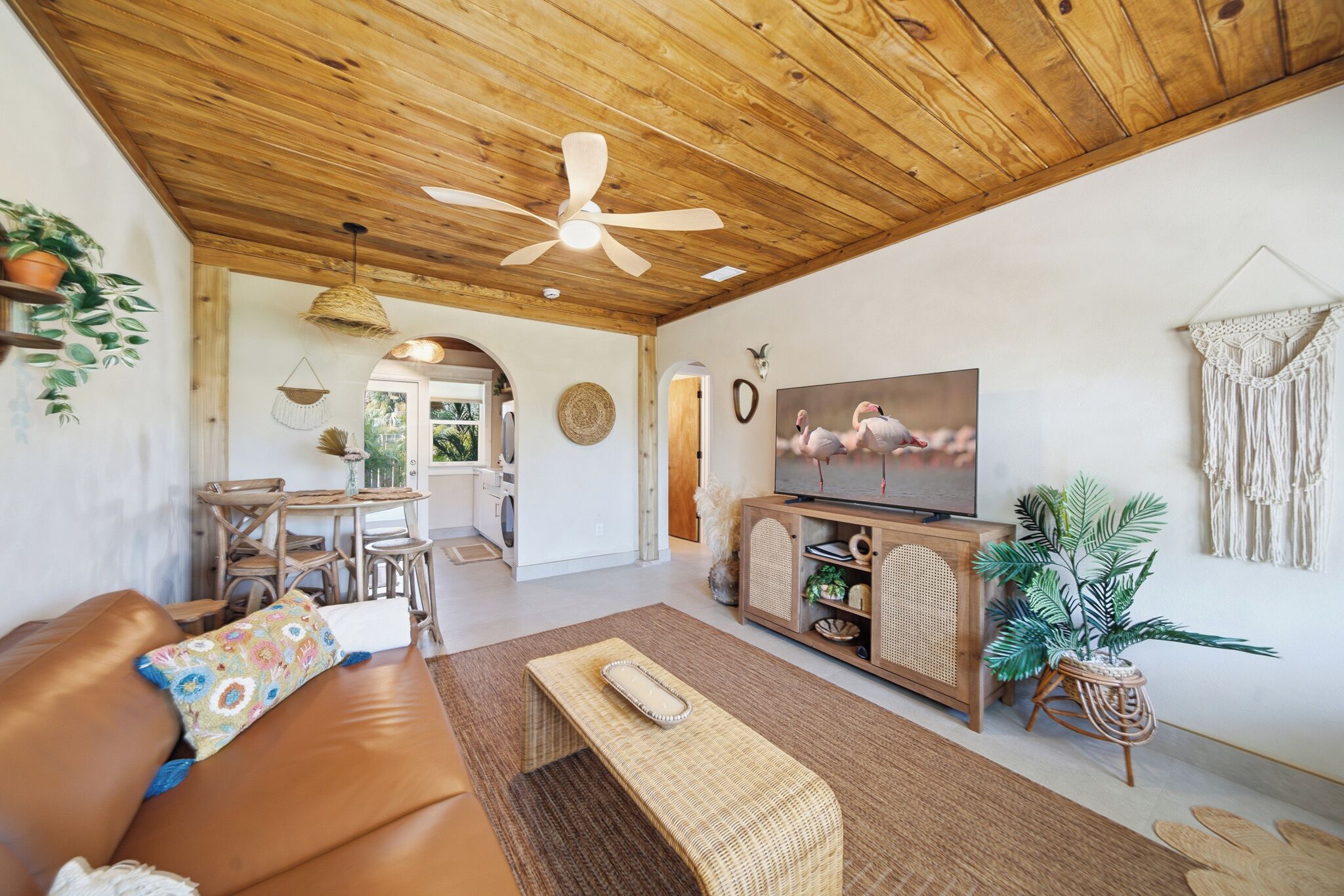 A cozy living room with a wooden ceiling, a television, a sofa, and a dining area.