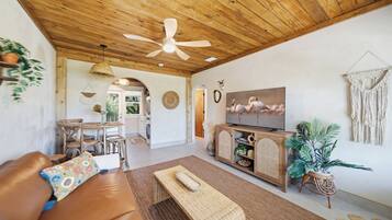 A cozy living room with a wooden ceiling, a television, a sofa, and a dining area.