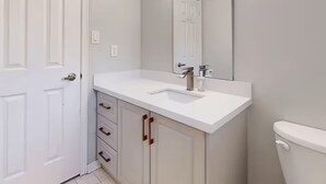 Casa de banho com lavatório branco, espelho e sanita.