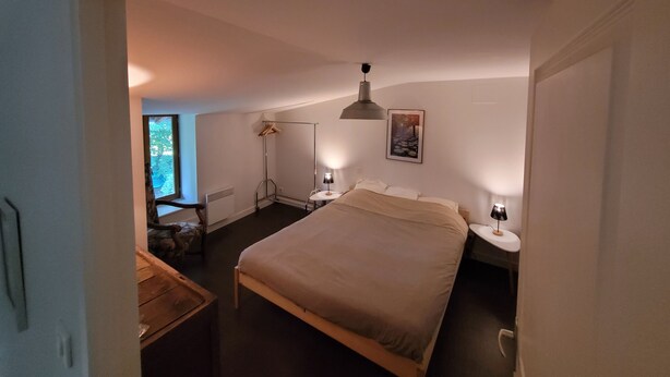 A bedroom with a large bed, bedside tables, a wardrobe, a radiator, and a window with a view of trees.