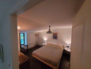 Ein Schlafzimmer mit einem großen Bett, Nachttischen, einem Kleiderschrank, einer Heizung und einem Fenster mit Blick auf Bäume.