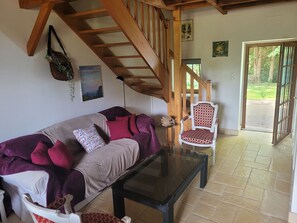 Ein Wohnzimmer mit einer Couch, einem Glastisch, einem gemusterten Sessel, einer Holztreppe und einer Tür, die nach draußen führt.