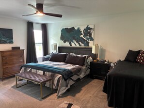 A bedroom with a bed, bedside tables, a dresser, a bench, a ceiling fan, and artwork on the walls.