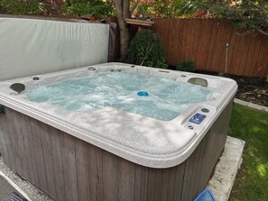 A hot tub with a control panel, surrounded by a wooden fence and greenery.