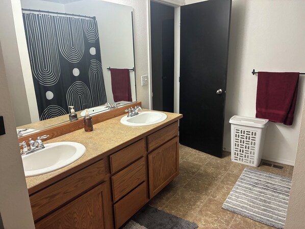 A bathroom with two sinks, a mirror, a towel rack, a laundry basket, and a patterned shower curtain.