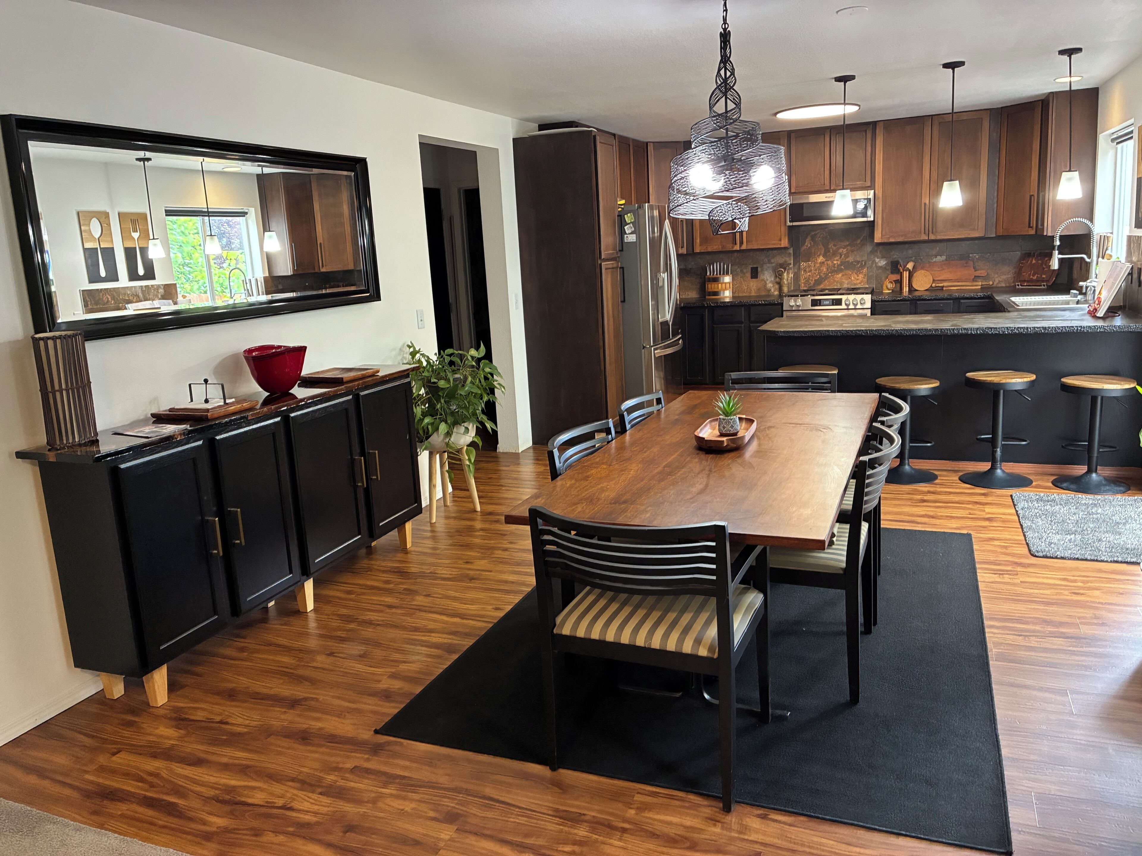 A modern kitchen with wooden cabinets, a dining table with chairs, and a hanging light fixture.