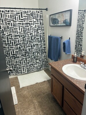 A bathroom with a patterned shower curtain, a sink with a soap dispenser, and towels on a rack.