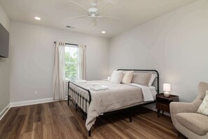A bedroom with a bed, a nightstand, a chair, a ceiling fan, and a window with curtains.