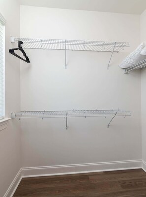 A room with a white wall, a wooden floor, and a metal drying rack.