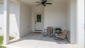 Eine überdachte Veranda mit Deckenventilator, zwei Stühlen, einem Blumentopf und einer Tür mit Fußmatte.