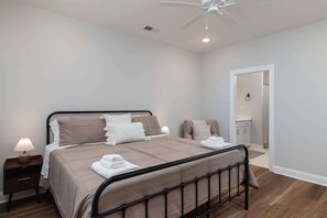 A bedroom with a bed, bedside tables, a ceiling fan, and a door leading to a bathroom. - The Oxford Escape | 3BR/3.5BA Near Ole Miss + M-Trade Park (Oxford)