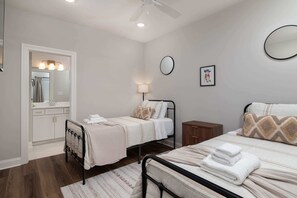 A bedroom with two beds, a bedside table, a nightstand, a mirror, and a wall clock.