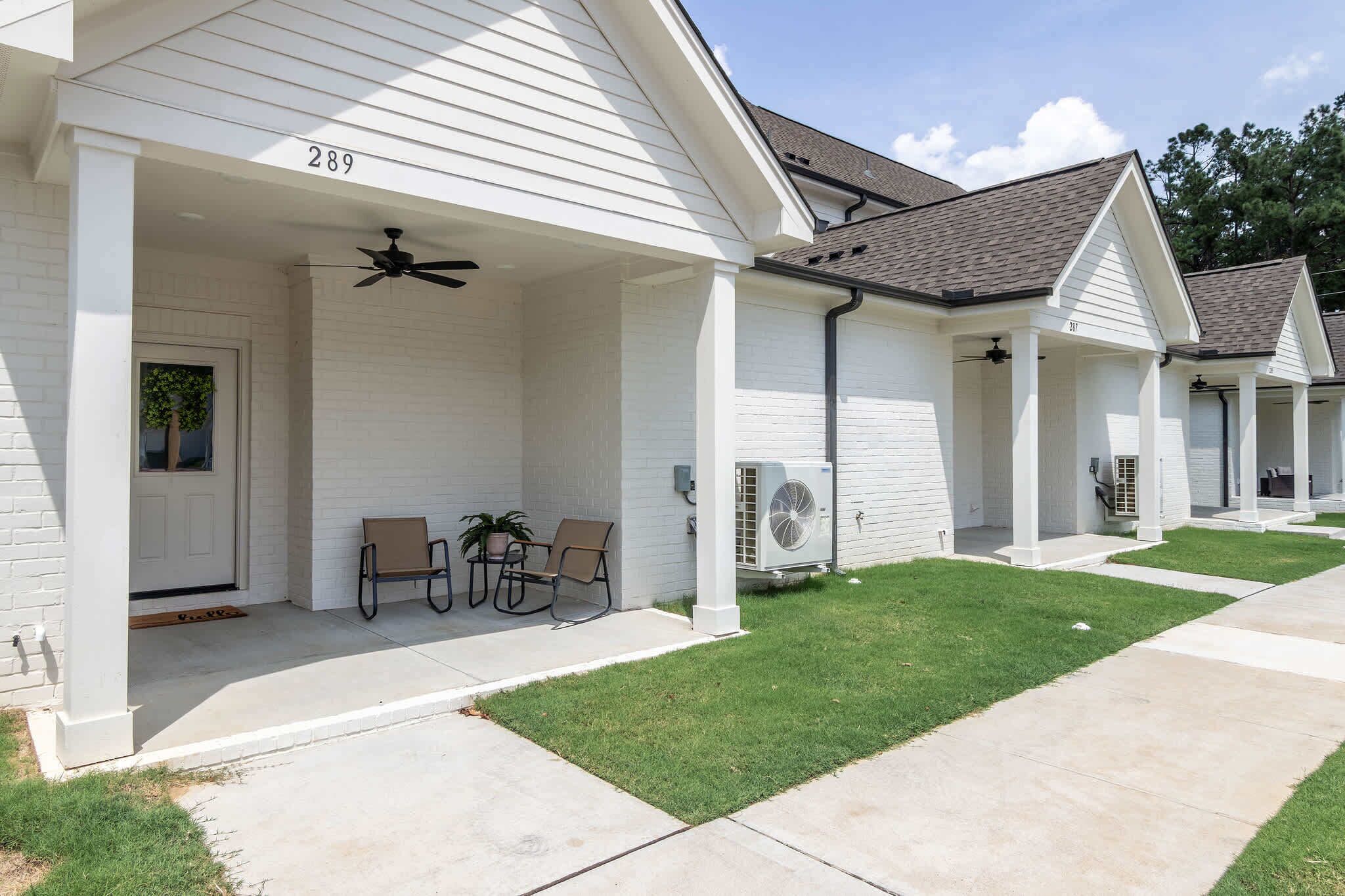 A row of single-story buildings with numbered doors, outdoor seating, and a covered porch area.