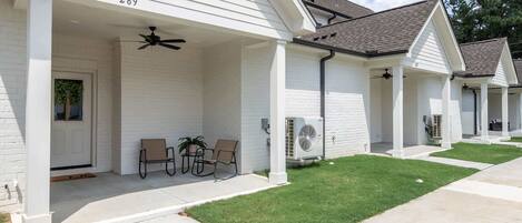 A row of single-story buildings with numbered doors, outdoor seating, and a covered porch area.