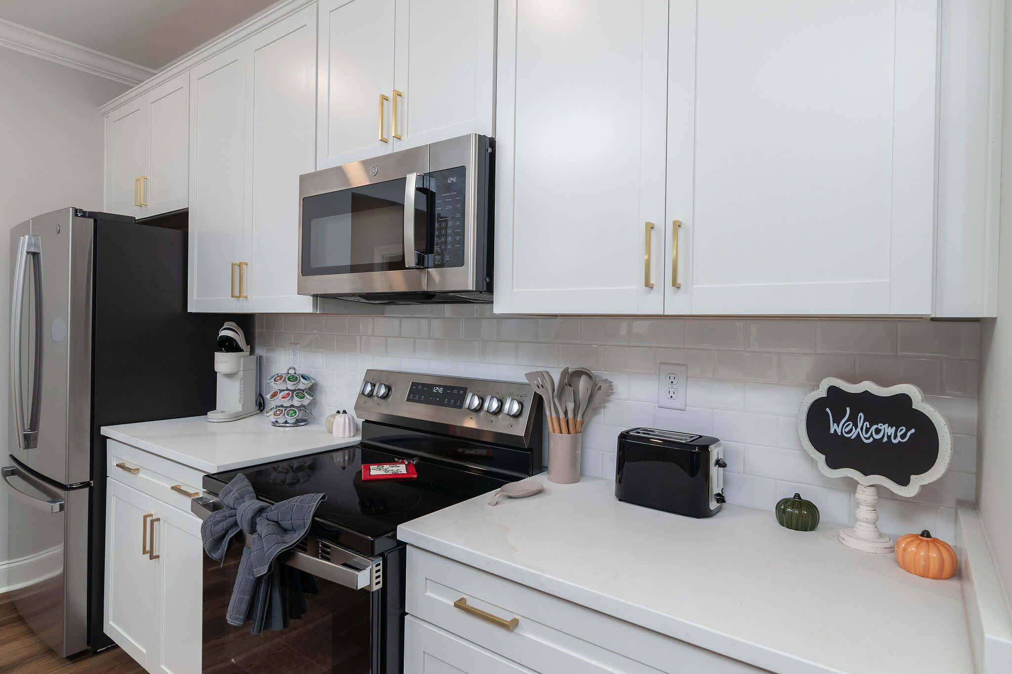 A modern kitchen with white cabinetry, stainless steel appliances, and a welcome sign.