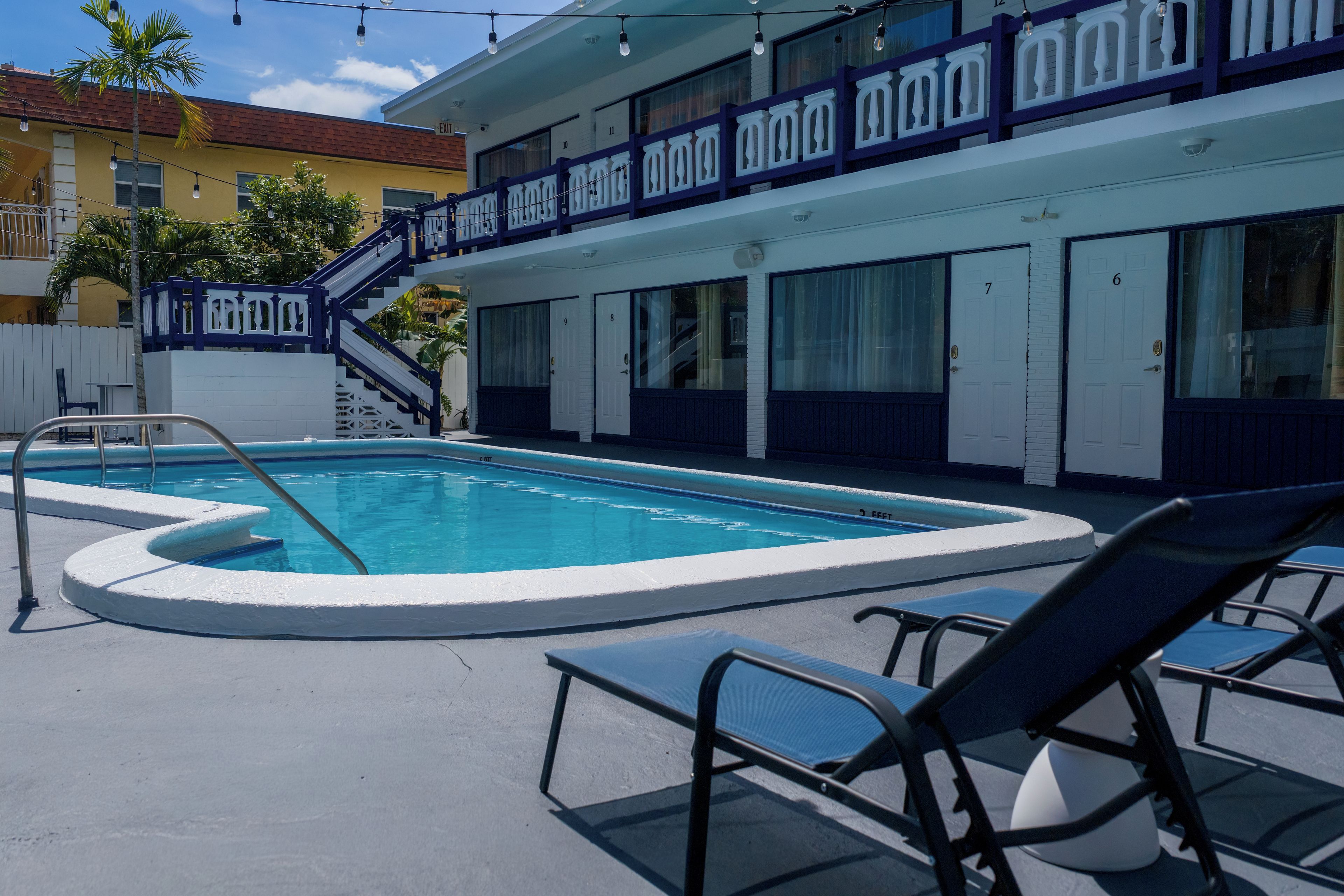 A swimming pool with lounge chairs, a staircase, and a building with numbered doors.