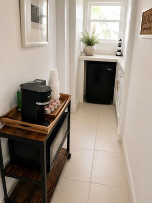 Una cocina con una cafetera, una bandeja con tazas, una planta en maceta y un cartel en la pared.
