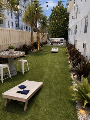Un patio al aire libre bien cuidado con césped, mobiliario y luces colgantes.
