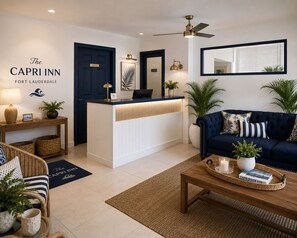A hotel reception area with a reception desk, a blue sofa, and a coffee table. - Beautiful Deluxe Queen Room (Fort Lauderdale)