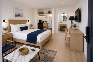 Ein modernes Hotelzimmer mit einem großen Bett, Nachttischen, einem Schreibtisch, einem Sessel sowie einem sichtbaren Badezimmer hinter einer geöffneten Tür.